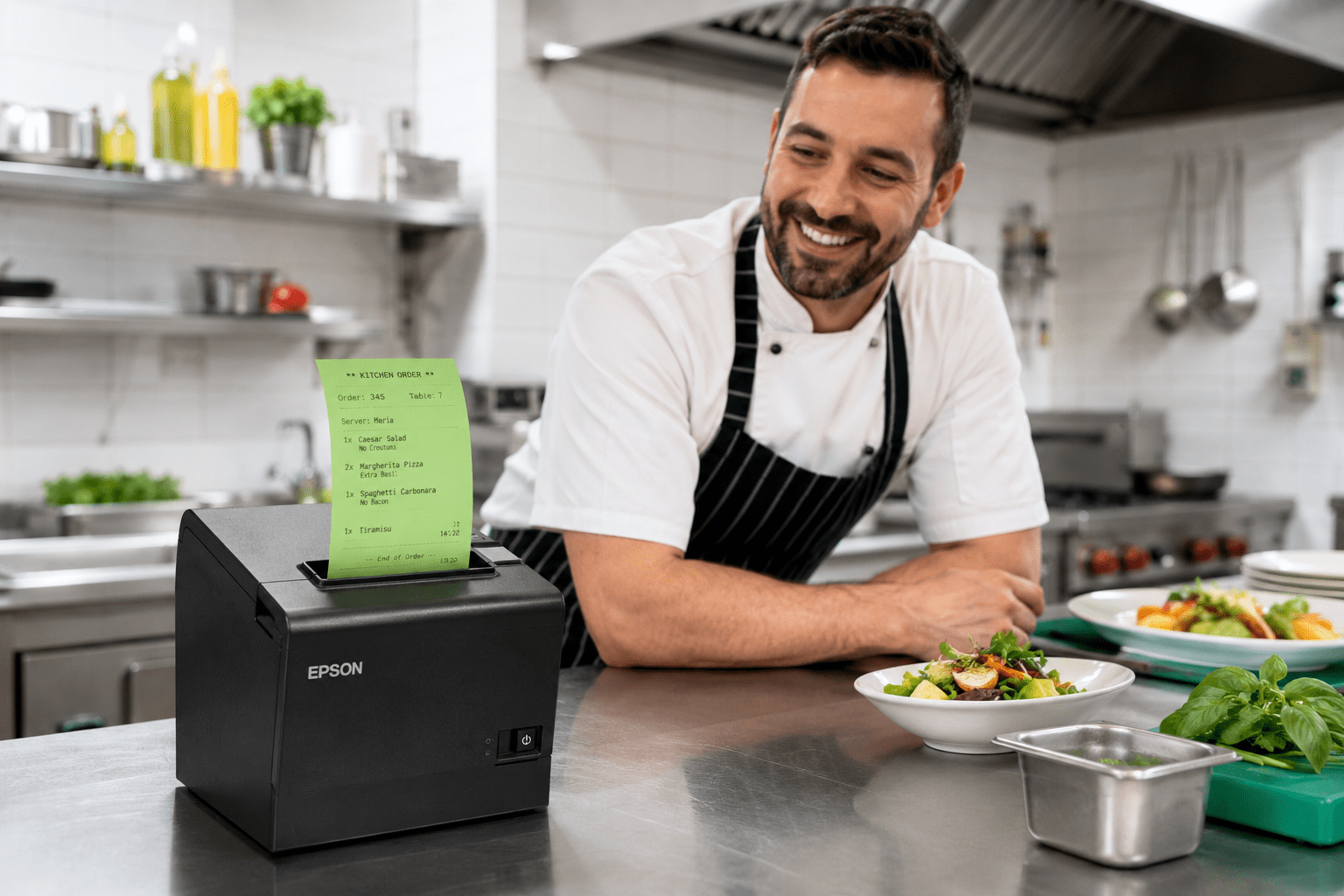 Impresora térmica de tickets imprimiendo una comanda de cocina de color en una cocina blanca, limpia y ordenada con un cocinero sonriente al fondo